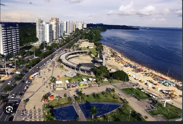 Vista aérea da Praia da Ponta Negra em Manaus, com o anfiteatro, a orla do Rio Negro, edifícios e trânsito na avenida